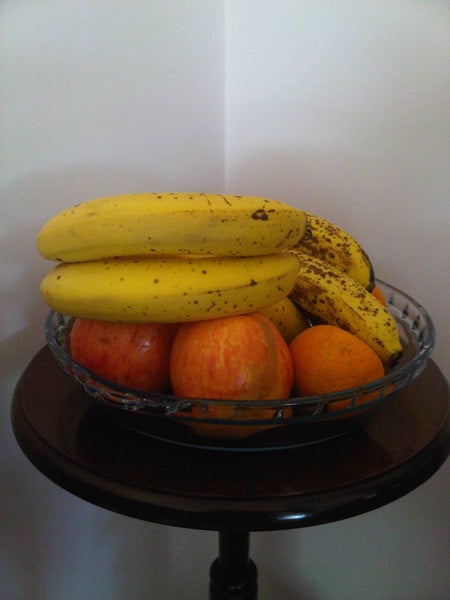 Fruit bowl with bananas, apples, and oranges on a table.