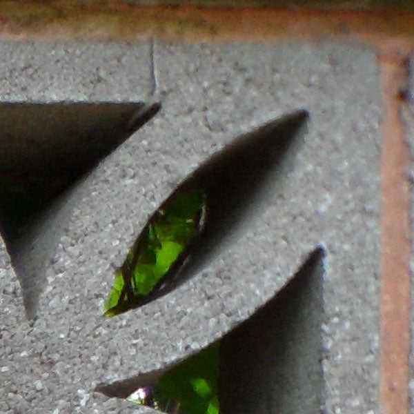 Close-up of a green gemstone through a carved stone aperture.