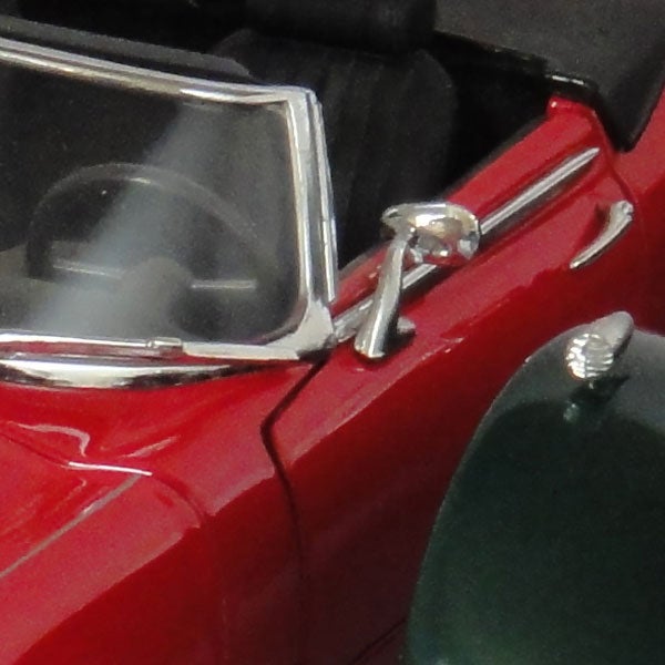 Close-up of a red vintage car model's side mirror and windshield.