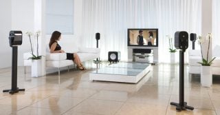 Woman sitting by Monitor Audio Apex speaker setup in living room.