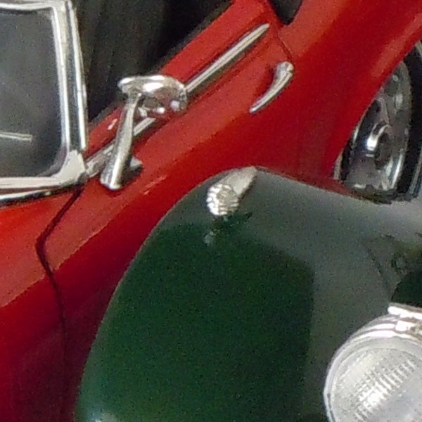 Close-up of a classic red car's mirror and headlight.