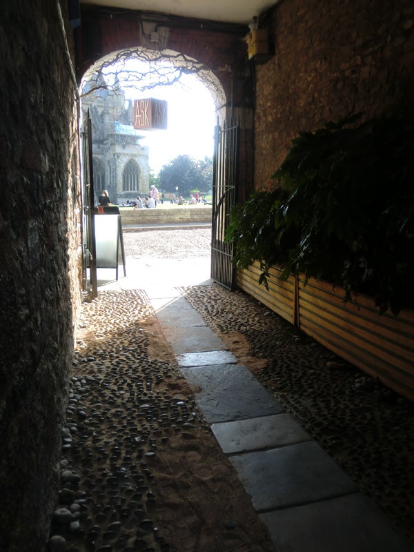 Cobbled alleyway leading to sunlit courtyard through arched entrance