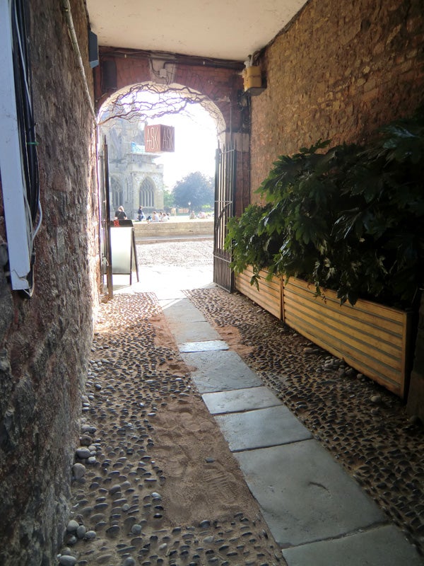 Cobblestone alleyway leading to a bright courtyard.