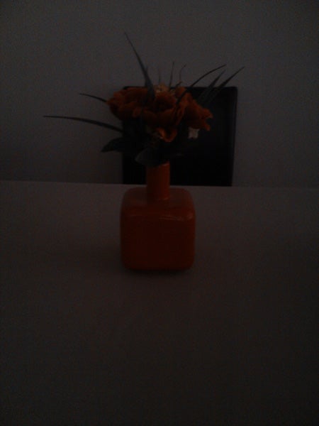 Orange vase with flowers on table in dim lighting.