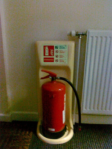 Fire extinguisher standing next to a radiator.