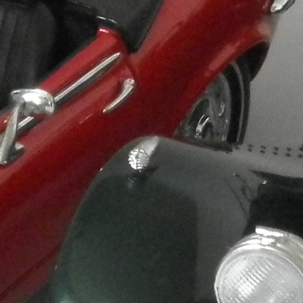 Close-up of a red toy car’s silver bumper and headlight.