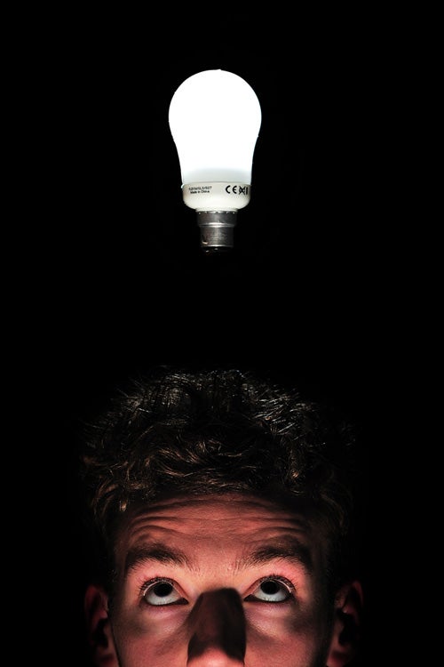 Man with illuminated light bulb above his head in darkness.