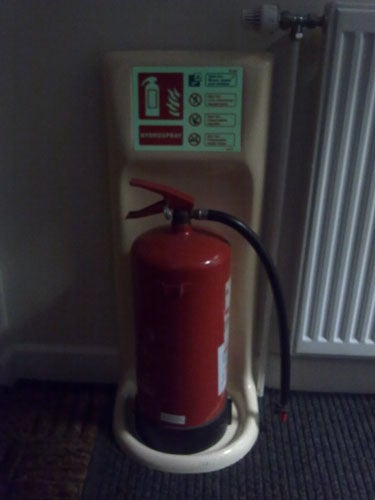 Fire extinguisher in a stand with information signs behind it.