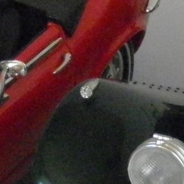 Blurred image of a red vehicle and part of a scooter.