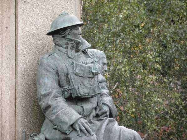 Bronze statue of a soldier with a helmet sitting against a wall