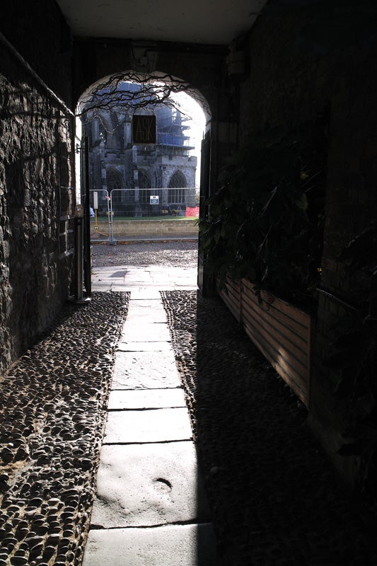 Cobbled alleyway with sunlight and shadows leading to archway.