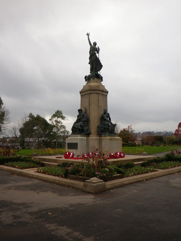 War memorial statue and wreaths with overcast sky.