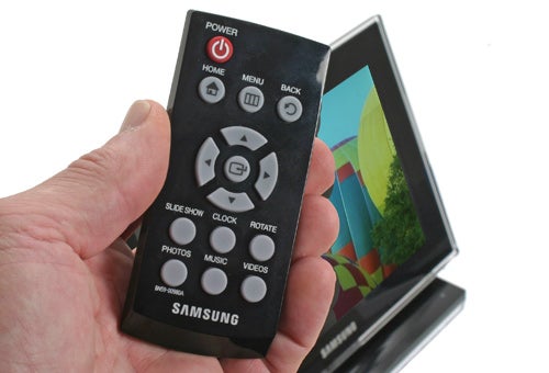 Hand holding a Samsung 1000P digital photo frame remote.