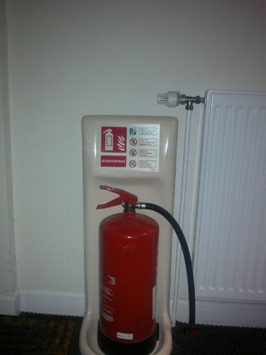 Fire extinguisher on stand next to a radiator.Fire extinguisher mounted on a wall beside a radiator.