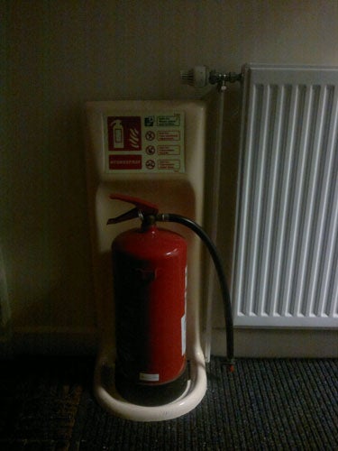 Fire extinguisher on stand next to a radiator.