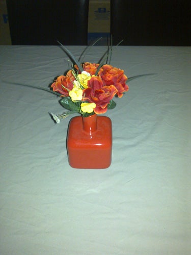 Artificial flowers in a red vase on a table.