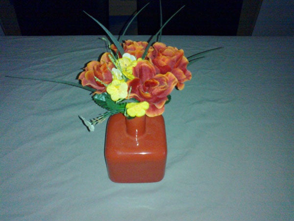 Artificial flower arrangement in an orange vase on a table.