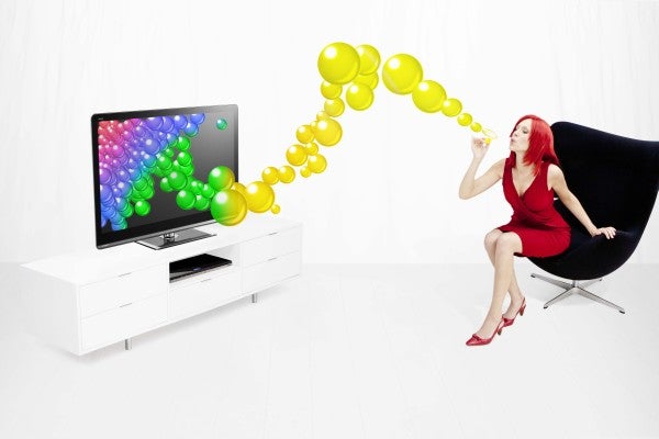 Woman blowing colorful bubbles towards a high-definition television.