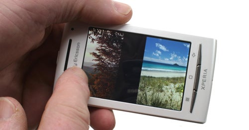 Hand holding a Sony Ericsson Xperia X8 displaying a landscape photo.