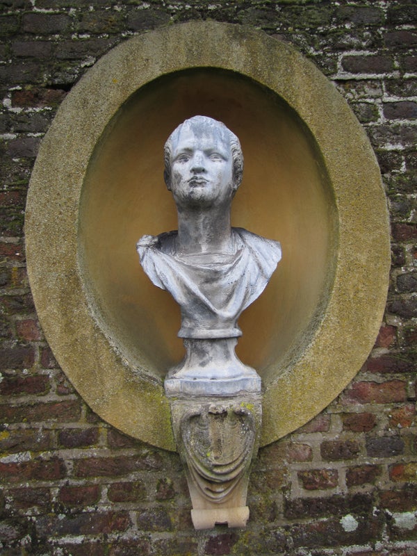 Stone bust in a circular wall niche with a brick background.