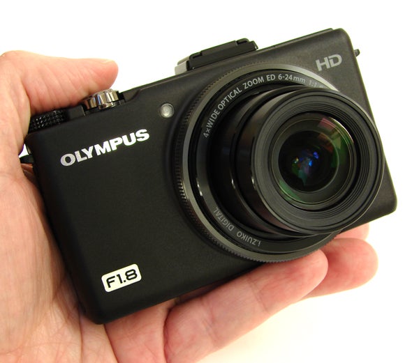 Hand holding Olympus XZ-1 digital camera with lens visible.