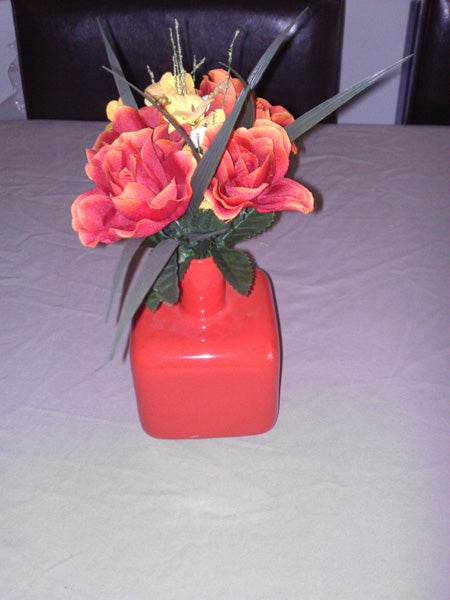 Bouquet of artificial roses in a red vase on a table.