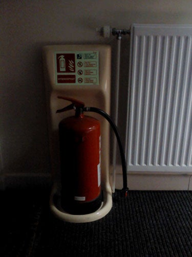 Fire extinguisher and stand beside a white radiator.