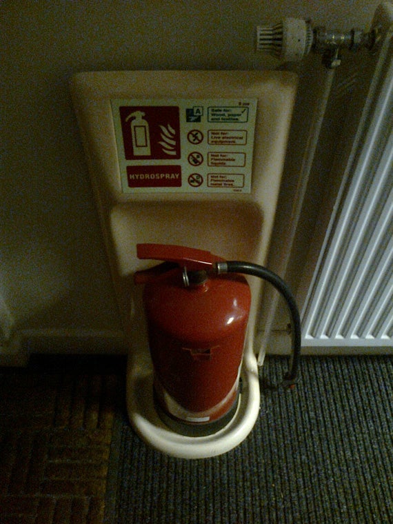 Red fire extinguisher mounted on wall with safety instructions.