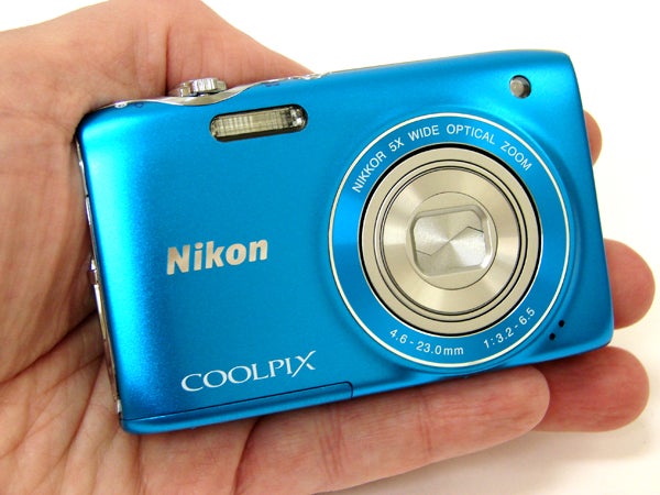 Hand holding a blue Nikon Coolpix S3100 camera.