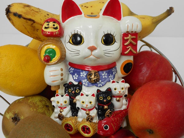 Maneki-neko figurines surrounded by assorted fruits.