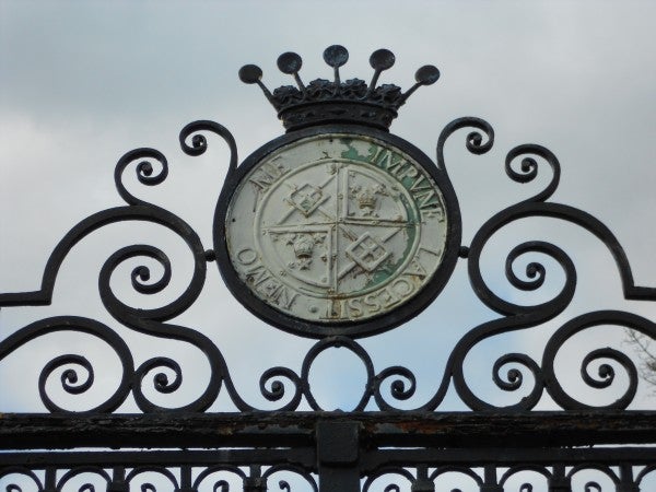 Ornate gate crest with weathered emblem against cloudy sky.