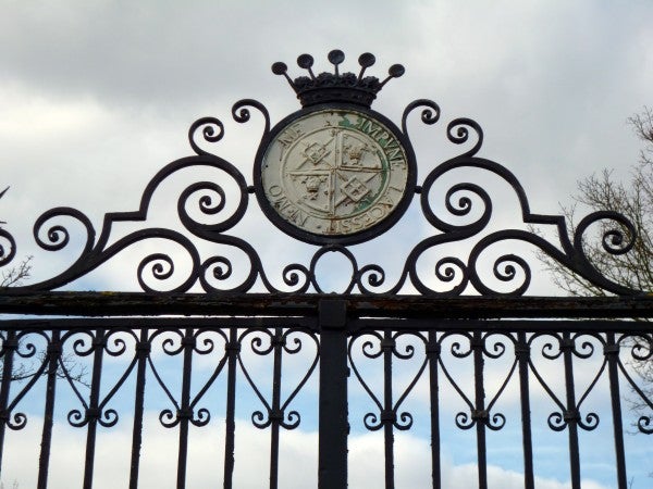 Ornate gate with clock and emblem under a cloudy sky.