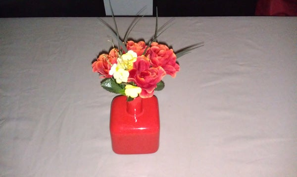 Bouquet of artificial flowers in a red vase on a table.