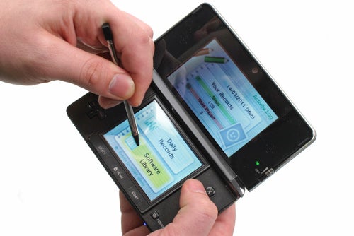 Hands holding a Nintendo 3DS and using a stylus on touchscreen.