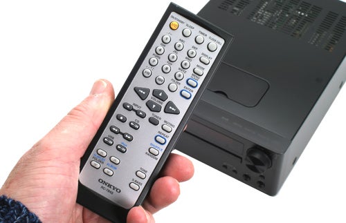 Hand holding Onkyo CS-545UK's remote control with unit in background.