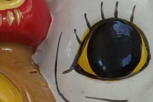 Close-up of a colorful ceramic figurine's eye detail.