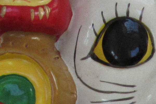Close-up of a colorful ceramic figurine's eye and mouth.