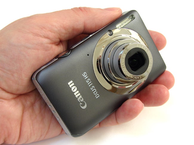 Hand holding a Canon IXUS 115 HS digital camera.