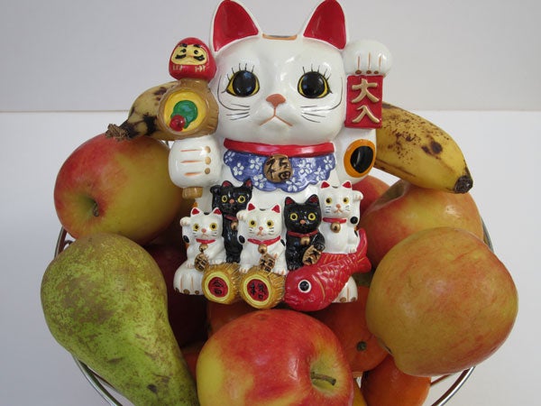 Maneki-neko figurines surrounded by assorted fruits in a bowl.