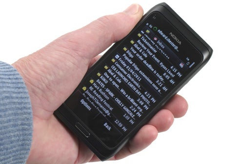 Hand holding a Nokia E7 smartphone displaying screen.