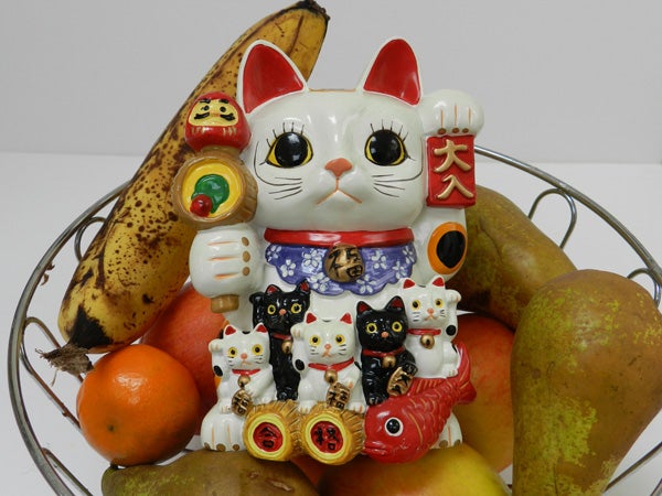 Colorful Maneki-neko figures surrounded by various fruits.
