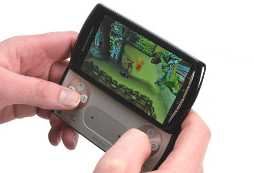 Hands holding a Sony Ericsson Xperia Play running a game.
