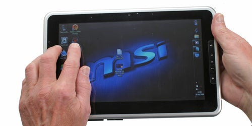 Hands holding an MSI WindPad 100W tablet displaying the desktop.