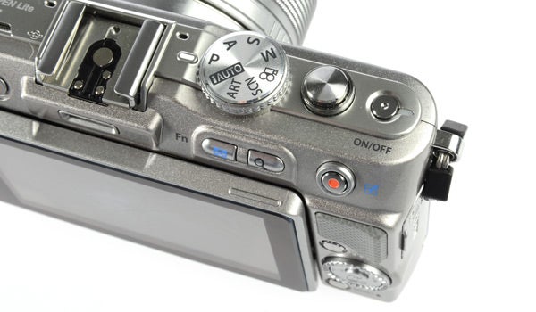 Olympus PEN E-PL3 camera with silver lens on white background.Olympus PEN E-PL3 camera with flip-out display screen.Olympus PEN E-PL3 camera with a zoom lens attached.Olympus PEN E-PL3 camera body next to detached lens.Close-up of Olympus PEN E-PL3 camera's top control dials.