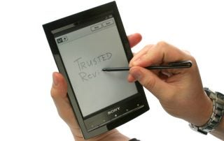 Hand holding Sony Reader PRS-T1 with stylus writing on it.