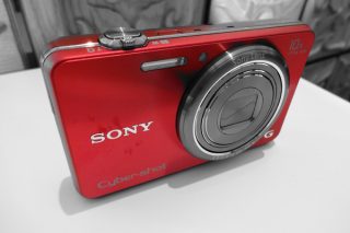 Red Sony Cyber-shot WX100 camera on a white surface.