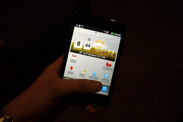Hand holding an LG Optimus Vu smartphone displaying the home screen.