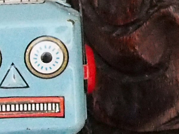 Close-up of a vintage robot toy beside a wooden object.