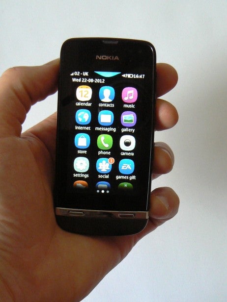 Hand holding Nokia Asha 311 showing home screen icons.