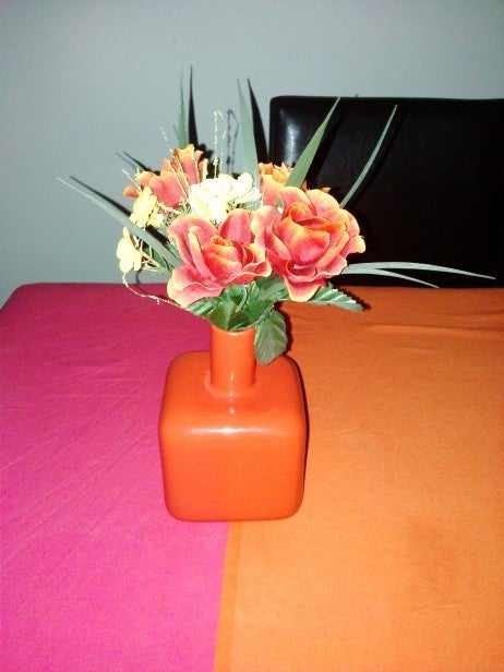 Artificial flower arrangement in red vase on table.